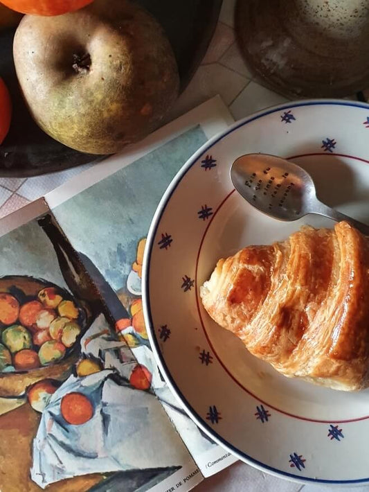 picture of an apple and a croissant on the dessert french vintage plate with a spoon and a vintage sezanne art book