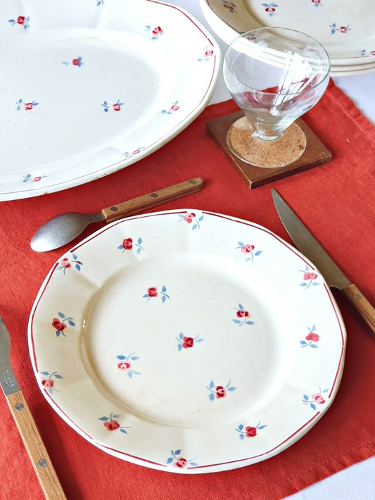 picture of a dining plating scene with a french vintage plate with small flowers print and red edge from Digoin-Sarreguemines and a vintage wood coaster with a art nouveau style wine glass on the red linen table cloth